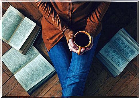 Woman drinking coffee sitting on the floor with books